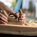 Handwerkerhände mit altem Holzhobel beim Abhobeln eines Hozbalk