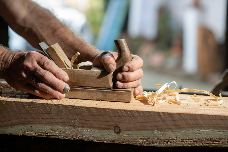 Handwerkerhände mit altem Holzhobel beim Abhobeln eines Hozbalk
